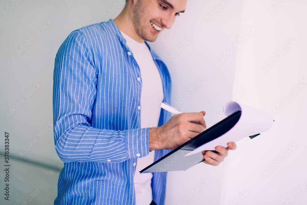Side view of cheerful male student analyzing course work report during learning time making idea notes of education information, joyful man in smart casual clothing enjoying studying process Side view of cheerful male student analyzing course work report during learning time making idea notes of education information, joyful man in smart casual clothing enjoying studying process