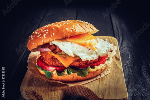 Beef burger with melted cheese and bacon and egg on wooden background