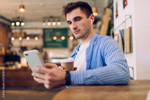 Thoughtful guy browsing phone while drinking coffee