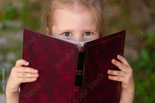 Φωτογραφία the child slyly narrowed his eyes and holds a book