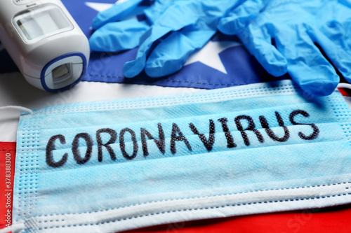 Word CORONAVIRUS written on protective mask, thermometer, gloves and American flag, closeup. Covid-19 pandemic in USA