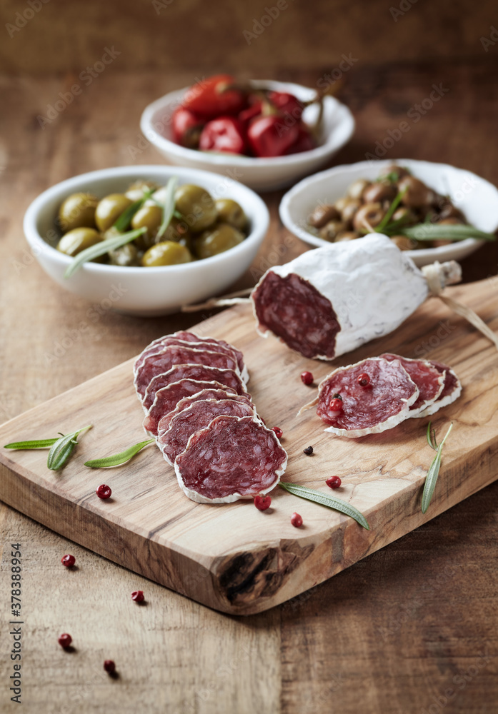 Sliced french salami with fresh rosemary and olives on rustic wooden background.