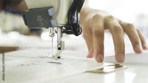 Hands and white cloth close up, sewing on machine. Digital machine, power button, female hands on white machine with blurry background