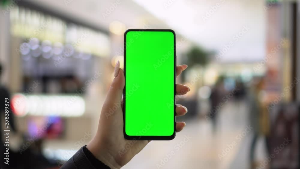 Shopping center. Back view of brunette holding chroma key green screen smartphone watching content. Gadgets and contemporary people concept. Shopping center. Back view of brunette holding chroma key green screen smartphone watching content. Gadgets and contemporary people concept.