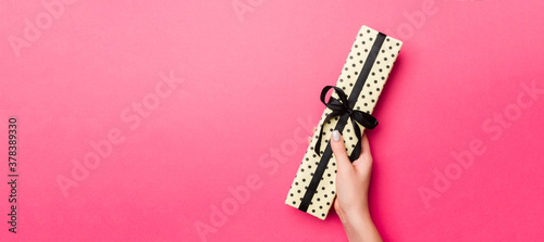 Girl Hands holding craft paper gift box with as a present for Christmas or other holiday on pink background, top view with copy sppace photo