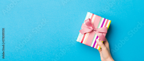 Woman arms holding gift box with colored ribbon on blue table background, top view and copy space for you design