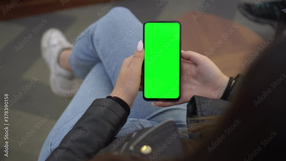 Shopping center. Back view of brunette holding chroma key green screen smartphone watching content. Gadgets and contemporary people concept. Shopping center. Back view of brunette holding chroma key green screen smartphone watching content. Gadgets and contemporary people concept.