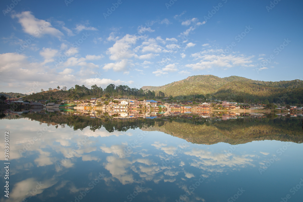 village on mountain reflection on water againts sky
