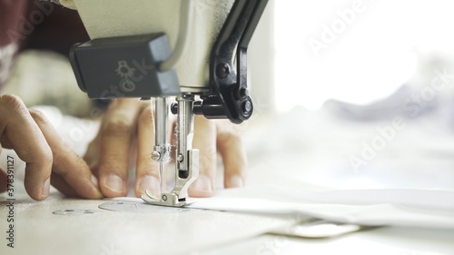 Hands and white cloth close up, sewing on machine. Digital machine, power button, female hands on white machine with blurry background