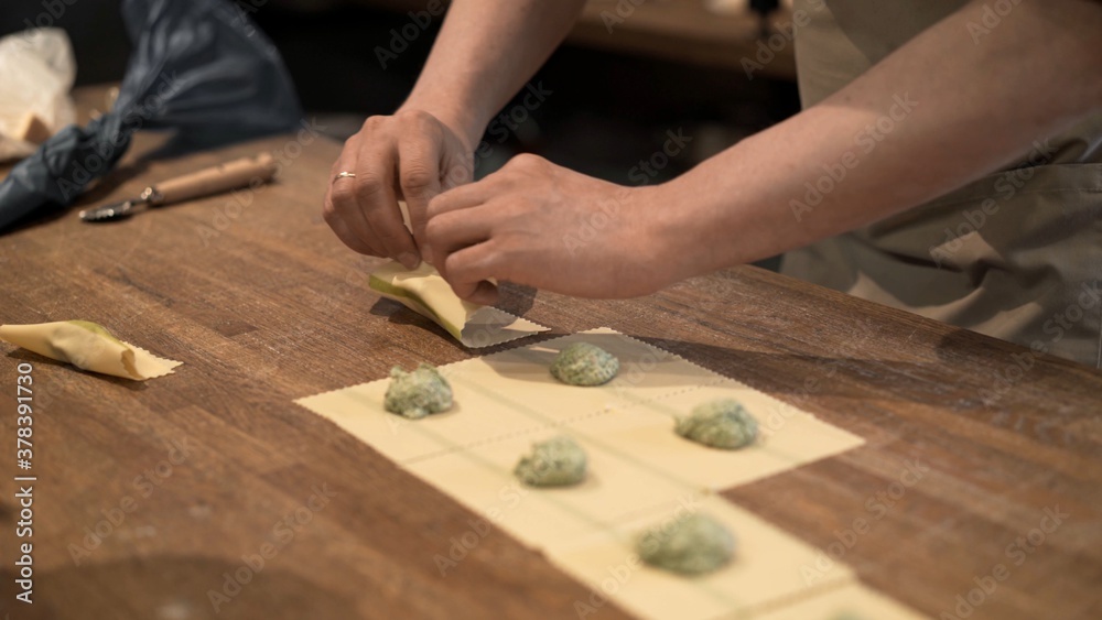 Cook preparing ravioli, rolling dough with stuffing on wooden kitchen table. Male hands cooking italian food, handmade ravioli at the restaurant kitchen