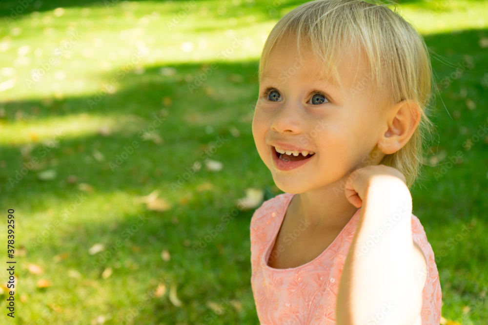 Portrait of cute beautiful blonde baby girl with big blue eyes and open mouth.Emotional little european girl happily surprised.Child standing isolated in the green park.Childhood concept Portrait of cute beautiful blonde baby girl with big blue eyes and open mouth.Emotional little european girl happily surprised.Child standing isolated in the green park.Childhood concept