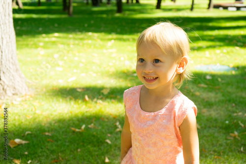 Portrait of cute beautiful blonde baby girl with big blue eyes and open mouth.Emotional little european girl happily surprised.Child standing isolated in the green park.Childhood concept © Hryhorii