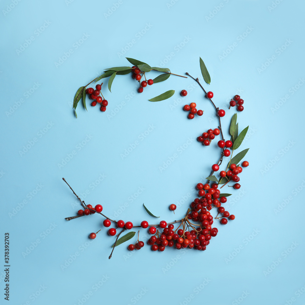 Red berries and leaves arranged in shape of wreath on light blue background, flat lay with space for text. Autumnal aesthetic - obrazy, fototapety, plakaty 
