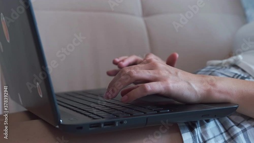 Women's hands close-up typing text on a laptop computer. A woman uses a laptop while lying on the sofa .