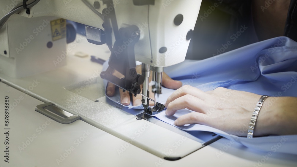 Sewing on machine, hands and blue cloth close up. Lens flare of sewing process, female hands on white machine with blurry effect side shot