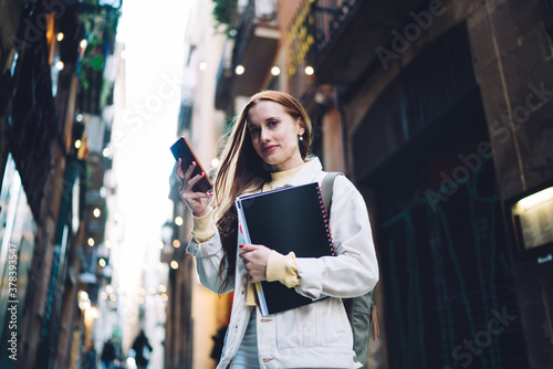 Positive modern female student texting on street