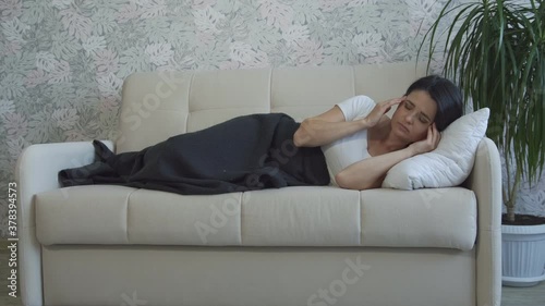 A young woman is resting on a sofa in a living room and wakes up from a headache, massaging her temples.