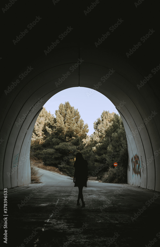 Image of a woman walking in a dark tunnel towards the camera