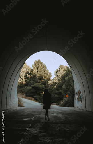 Image of a woman walking in a dark tunnel towards the camera