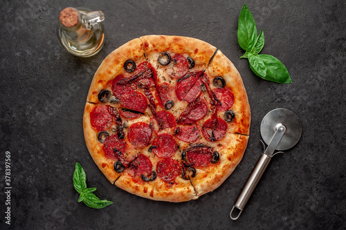 pizza pepperoni with salami sausages, mozzarella, olives, Provencal herbs, signature tomato sauce on a stone background