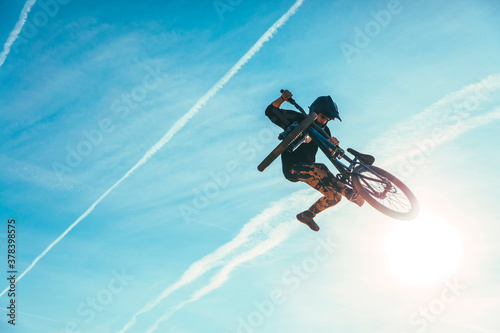 Carefree man jumping while performing stunt with bicycle against blue sky during sunset