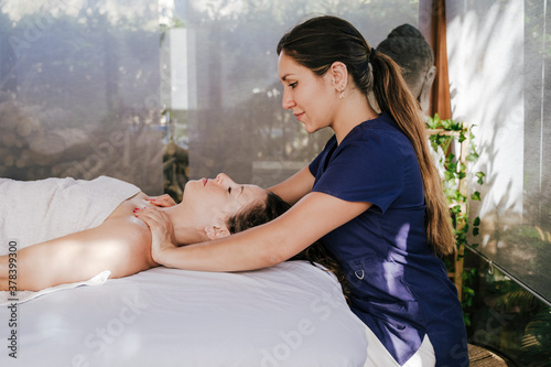Mid adult woman massaging female customer's neck lying on table in spa