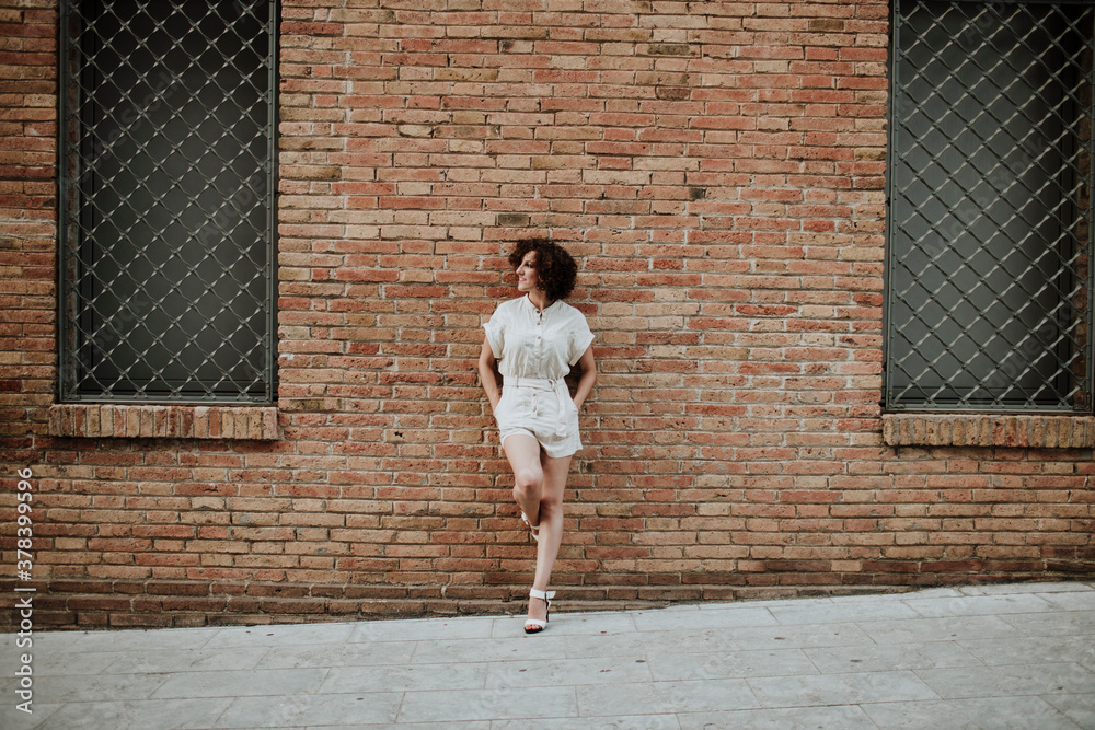 Mid adult woman with curly hair leaning on brick wall in city Mid adult woman with curly hair leaning on brick wall in city