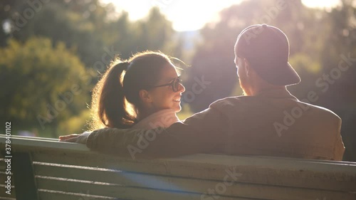Back view of young loving couple having date on bench in park