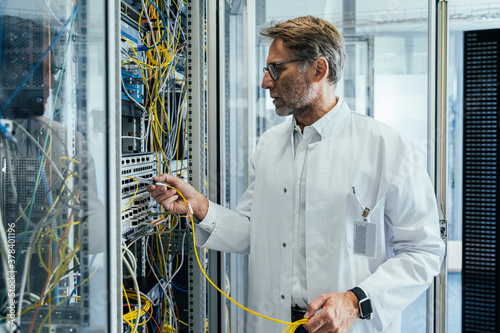 Mature man plugging transceiver on fiber optic cable into rack photo