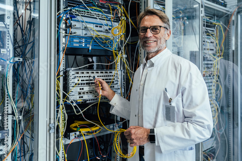 Smiling mature man plugging transceiver on fiber optic cable in data center