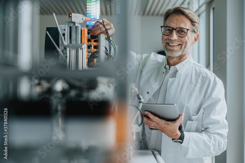 Smiling mature man with digital tablet inventing machinery in laboratory photo