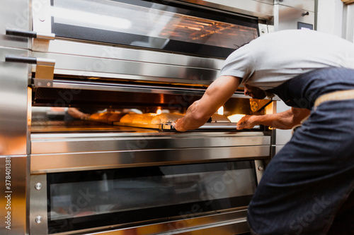 Baker baking bread in oven at bakery