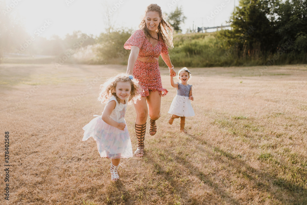 Happy mother running with daughters on a meadow in backlight