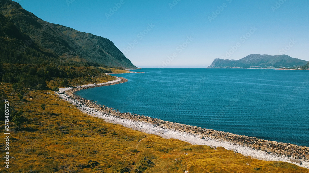 Coastline with mountains. Grassy slope and emerald water.