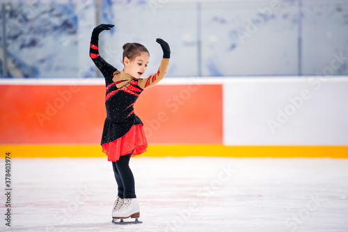 Obraz na plátně little girl figure skater in light pink tracksuit with smile skates on the ice on an indoor skating rink