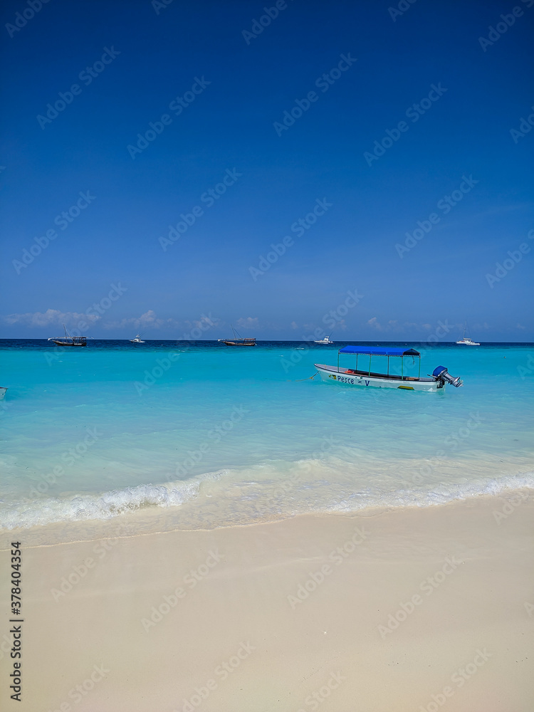 Zanzibar, Tanzania - December 3, 2019: Nungwi beach in Zanzibar, bright blue sea and blue sky on a beautiful white beach. The sailors' boats are on the shore for fishing and recreation. Vertical