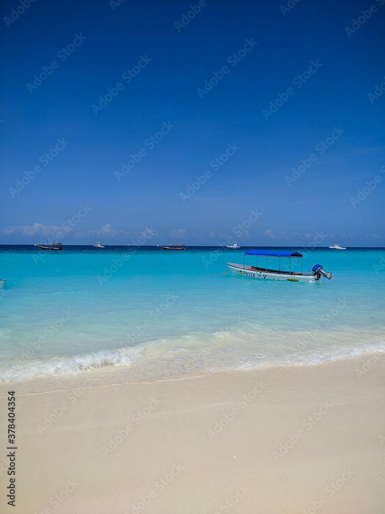 Obraz premium Zanzibar, Tanzania - December 3, 2019: Nungwi beach in Zanzibar, bright blue sea and blue sky on a beautiful white beach. The sailors' boats are on the shore for fishing and recreation. Vertical