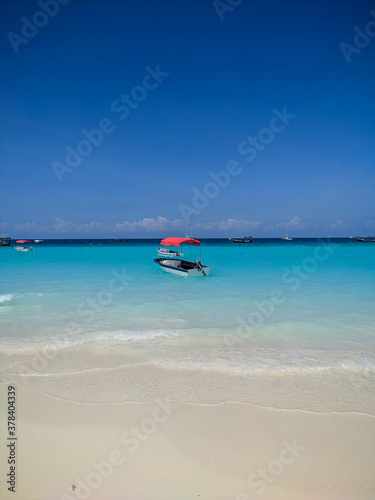 Fototapeta Naklejka Na Ścianę i Meble -  Zanzibar, Tanzania - December 3, 2019: Nungwi beach in Zanzibar, bright blue sea and blue sky on a beautiful white beach. The sailors' boats are on the shore for fishing and recreation. Vertical