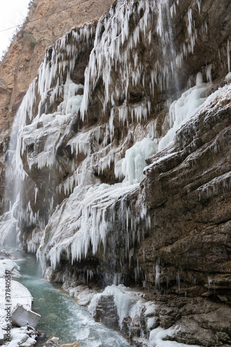 Vertical image of winter river and rozen icicles of big waterfall. Scenery winter landscape.