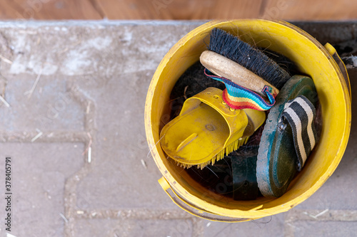 Bucket full of horse brushes. Curry comb, dandy brush, comb and body brush. Grooming kit for horses and ponies at the stable. Horse cleaning concept. Top down view, closeup, copy space.