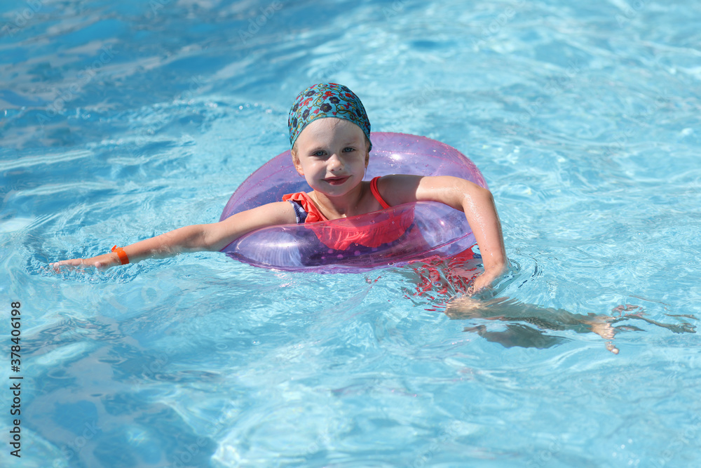 Beautiful girl swim in blue pool with inflatable ring. Professional swimming training for children.