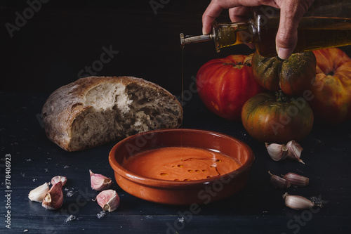 Still life of Salmorejo in a clay plate accompanied by the ingredients with which it is prepared: bread, tomato, garlic and olive oil. Darkfood style photography with matte finishes. photo