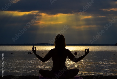 silhouette of a young woman practicing yoga on the beach at the sunset