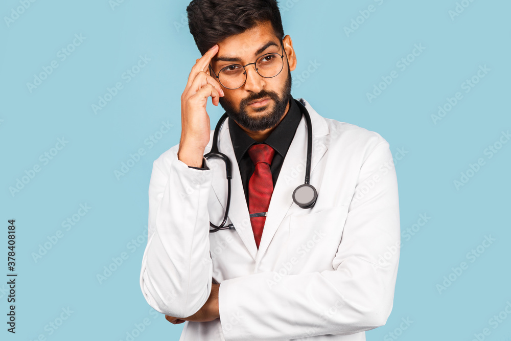 Cute Indian / Asian doctor wearing glasses with stethoscope, tie and white coat on light blue background.