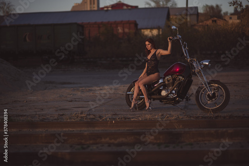 Fototapeta Naklejka Na Ścianę i Meble -  Beautiful sexy woman in lace bodysuit and high heels sits on a motorcycle on an industrial background