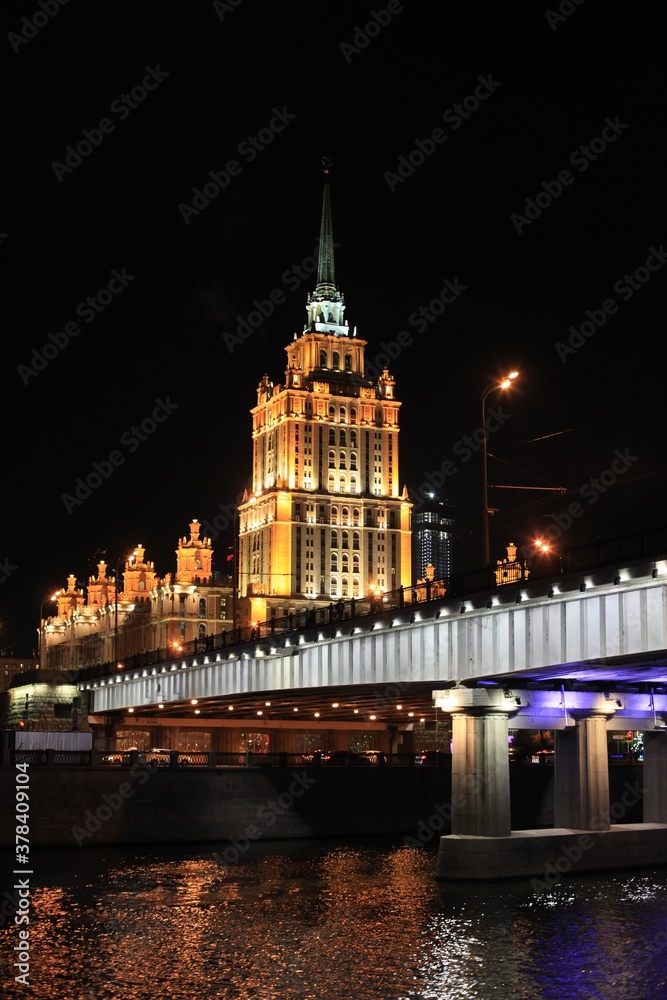 Fototapeta premium Colorful panorama of the night city with neon lights. Bridge over the river against the background of historic buildings at night
