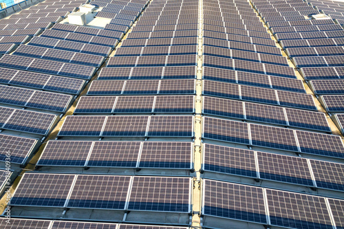 Aerial view of many photo voltaic solar panels mounted of industrial building roof.