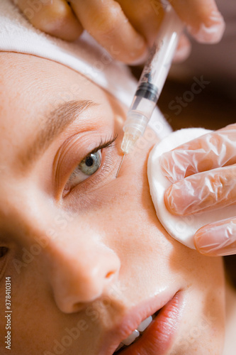 Portrait of a red-haired girl at a beautician's reception. Syringe, needle