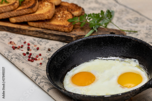 Fried eggs in a rustic iron pan, toast on a wooden board and a cup of coffee for breakfast.
