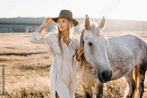 Картината върху платно Young woman cowgirl with white horse standing at a farm.